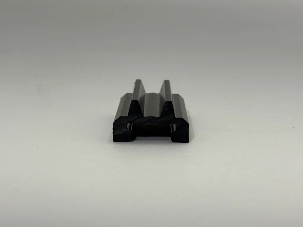 Close-up of a small, dark metal object with toothed gray jaws sitting on a light surface.
