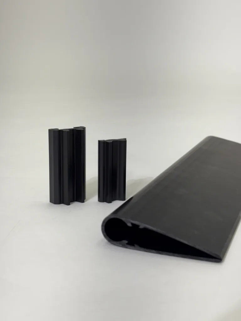 Three tall black ribbed posts stand on a light surface with a rolled black sheet to the right against a plain background.